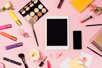top view of digital tablet and smartphone with blank screen, notebooks, flowers and decorative cosmetics on pink