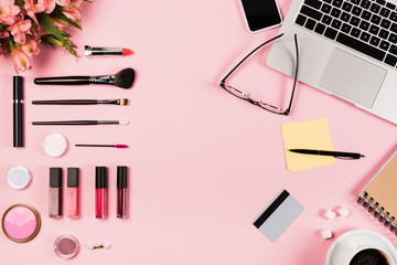 top view of laptop, smartphone with blank screen, cup of coffee, credit card, glasses, flowers and decorative cosmetics on pink