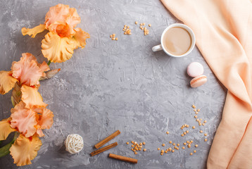 Orange iris flowers and a cup of coffee on a gray concrete background.