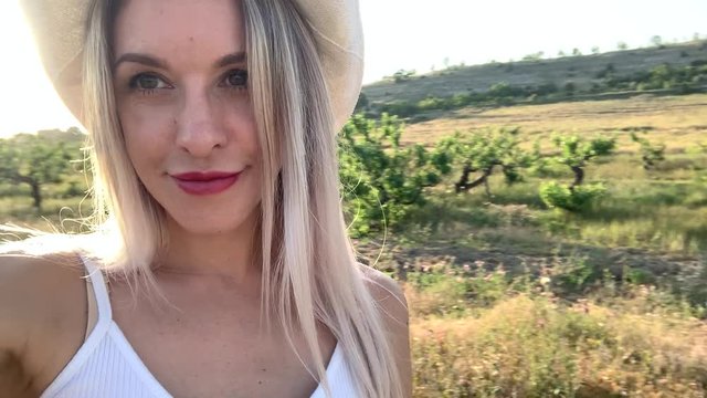 Beautiful blonde woman in a hat on the background of beautiful garden at sunset