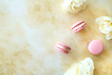 Feminine composition with traditional french macarons sweets and tender bicolor tulip flowers on yellow concrete textured background. Top view, close up, copy space.