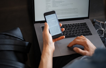 man working at the laptop sitting on the floor with smartphone and coffee in his hands