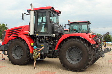 Obraz premium The boy climbs the stairs of a new big red tractor with large wheels at the exhibition of agricultural machinery