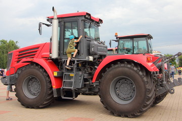The boy climbs the stairs to the cockpit of a large new red tractor with big wheels at the exhibition of agricultural machinery