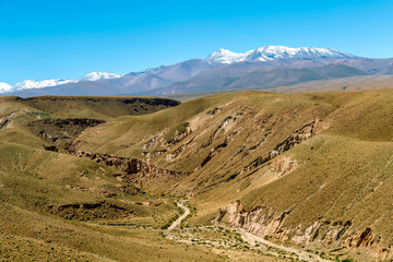 Fototapeta na wymiar Blurred background of Atacama Desert landscape with snow-capped Andean volcanos, salt flat and some vegetation on horizon, Chile