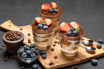 Classic tiramisu dessert with blueberries and strawberries in a glass on dark concrete background
