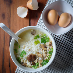 Pork boiled rice with shiitake mushrooms in a white tile cup on a wooden table. Beside there are eggs