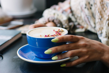 Coffee cup with latte art on wooden background in female hands. Beautiful foam, brown ceramic cup, space for text and design.