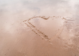 minimalist image of a large heart drawn in the sand placed to the right on a flat beach with blue sky reflecting in sand wet from receding water