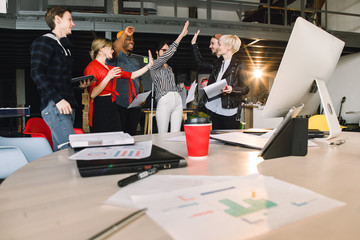 Young male and female colleagues working with project cooperating each other during meeting in office. Group of casually dressed businesspeople celebrating success