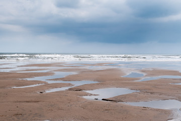 minimalist image of a flat sandy beach at Filey, North Yorkshire, with numerous puddles left behind by a low tide, with heavy grey clouds reflecting in the puddles