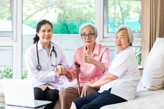 Family doctor or nurse wearing white coat and stethoscope with smiling senior patient during home visit,female caregiver,health visitor holding asian elderly woman hand,healthcare medicine concept