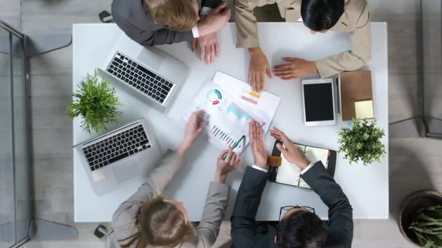 Directly above view of four businesspeople sitting at table, having conversation and then shaking hands to each other