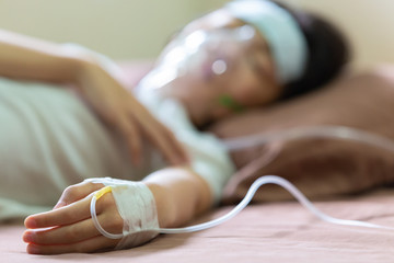 Asian little girl with cold gel placed on her forehead to relief fever and oxygen mask,hand of cute...
