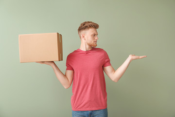 Young man with cardboard box on color background