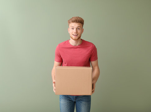 Young man with cardboard box on color background