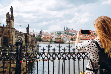 A girl with a backpack makes a photo on the phone of the Charles Bridge of Prague. Tourist girl...