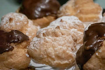 powdered sugar and shiny chocolate glased cream puffs with a swirl of white whipped cream