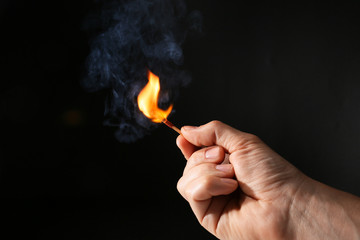 Male hand with burning match on dark background