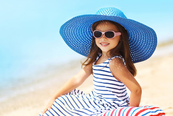 Summer holidays, vacation concept - portrait beautiful little girl in straw hat, striped dress relaxing on beach near sea