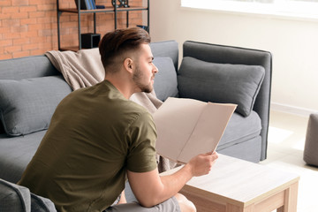 Handsome man reading newspaper at home