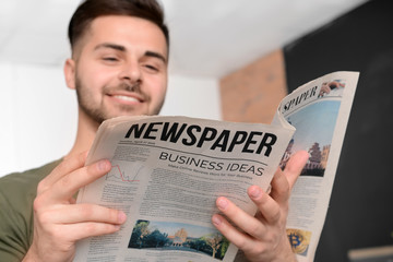 Handsome man reading newspaper at home