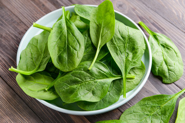 Plate with fresh spinach on wooden table