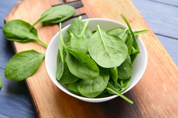 Bowl with fresh spinach on wooden board
