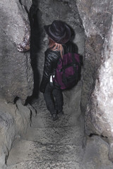 Girl exploring huge cave. Adventure traveller dressed cowboy hat and backpack, leather jacket....