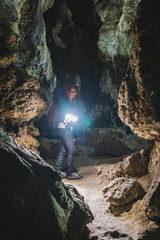 Girl exploring huge cave. Adventure traveller dressed cowboy hat and backpack, leather jacket. extreme vacation, tourist route. ancient crystal formations, vertical photo, village Kryvche. Ukraine