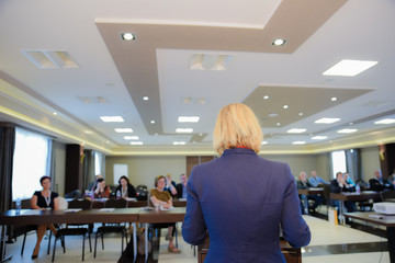Wider image of educational conference where female lecturer is facing the audience and presenting...