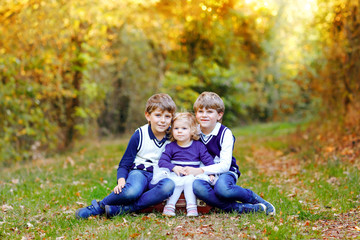 Naklejka na ściany i meble Portrait of three siblings children. Two kids brothers boys and little cute toddler sister girl having fun together in autumn forest. Happy healthy family playing, walking, active leisure on nature