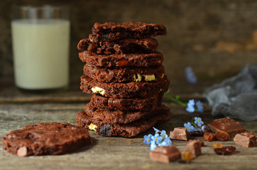 Chocolate cookies with nuts stacked. A glass of milk in the background