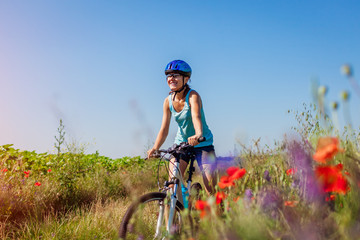 Happy young woman cyclist riding a mountain bicycle in summer field. Girl having fun lifting legs