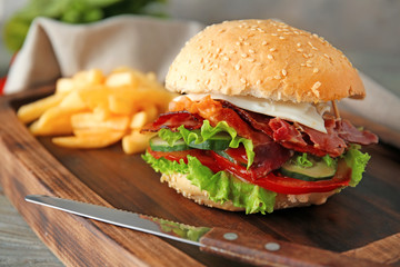 Tasty burger with bacon and french fries on table