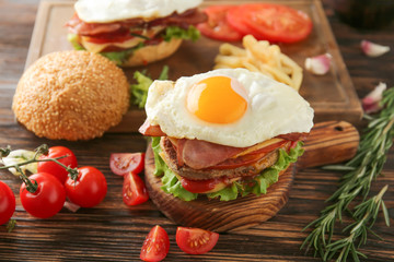 Tasty burgers with bacon and eggs on table