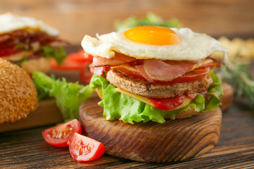 Tasty sandwich with bacon and fried egg on table