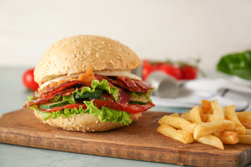Tasty burger with bacon and french fries on table