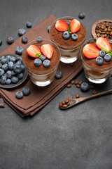 Classic tiramisu dessert with blueberries and strawberries in a glass on dark concrete background