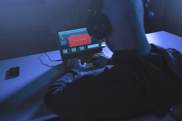 cybercrime, hacking and technology concept - male hacker in headphones with access denied message on laptop computer screen using virus program for cyber attack in dark room