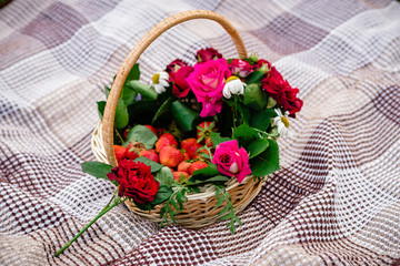 wicker basket with roses, flowers and red ripe strawberries on a checkered rug