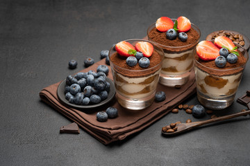Classic tiramisu dessert with blueberries and strawberries in a glass on dark concrete background