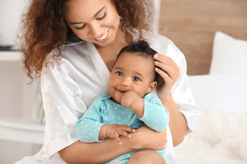 Happy African-American mother with cute little baby in bedroom