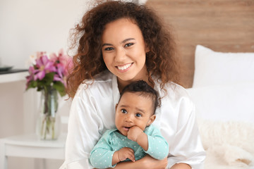 Happy African-American mother with cute little baby in bedroom