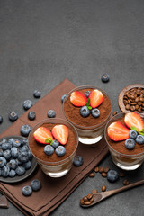 Classic tiramisu dessert with blueberries and strawberries in a glass on dark concrete background