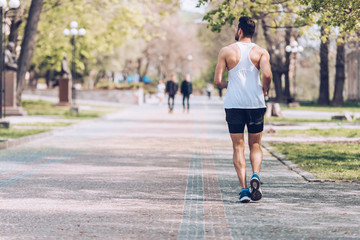 Obraz premium back view of young sportsman running along wide park alley
