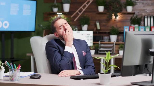 Exhausted office worker yawning while typing on the computer in modern and nice looking work space