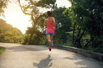 Fototapeta premium Sporty young woman in sportswear trail running on forest mountain path. Fitness girl jogging in Hong Kong