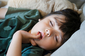 Toddler boy biting his finger nails while sleeping on sofa, Emotional child portrait, Child putting finger in his mouth lying on cooch, Kid taking a peaceful nap