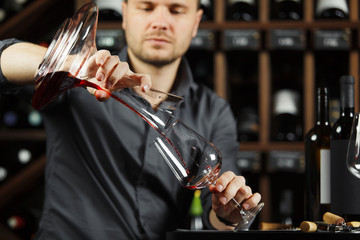 Sommelier pouring wine into glass from mixing bowl. Male waiter